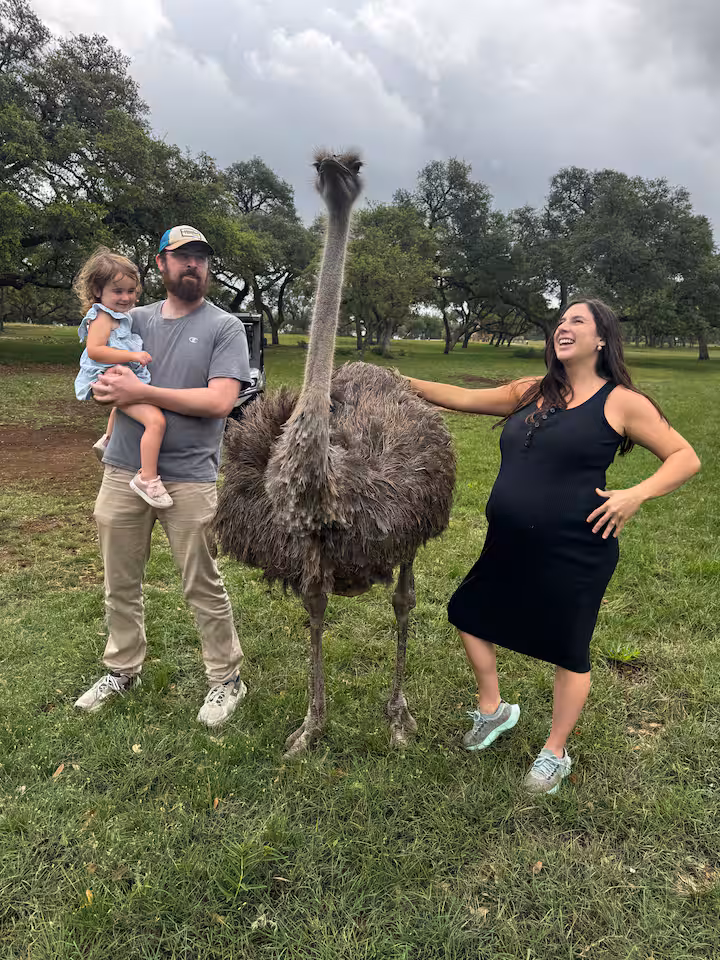 Family posing beside an ostrich in the pasture
